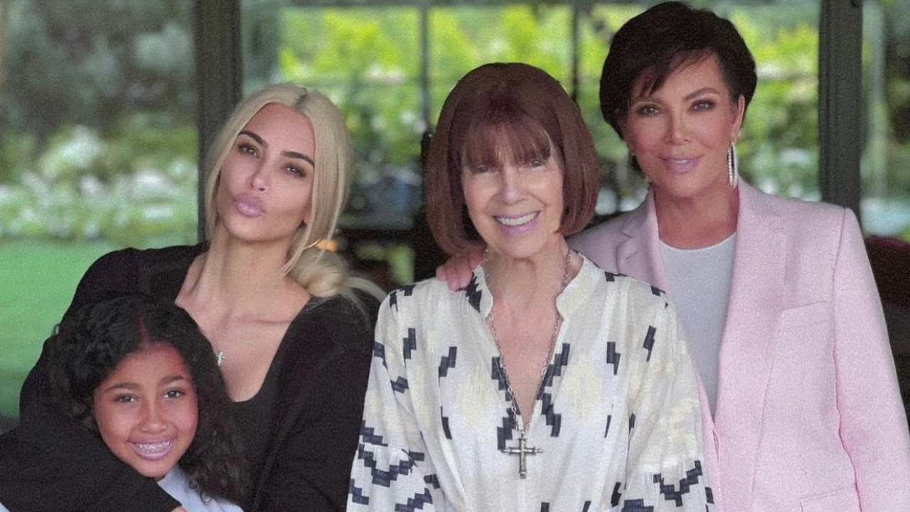 This photo shows Kim, her daughter, Mary Jo and Kris posing together smiling. They are standing by some bright pink flowers. 