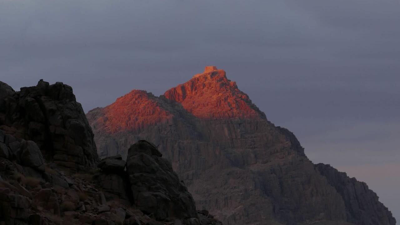 The peak of Mount Sinai at dusk in 2024. The light catches the top of the rocky mountain, which is standing higher than another mountain in the foreground