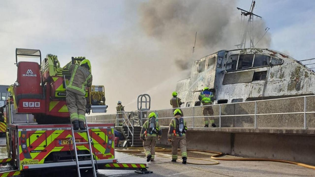 Firefighters putting damping down a fire on the Royal Iris boat with smoke still billowing out of it.
