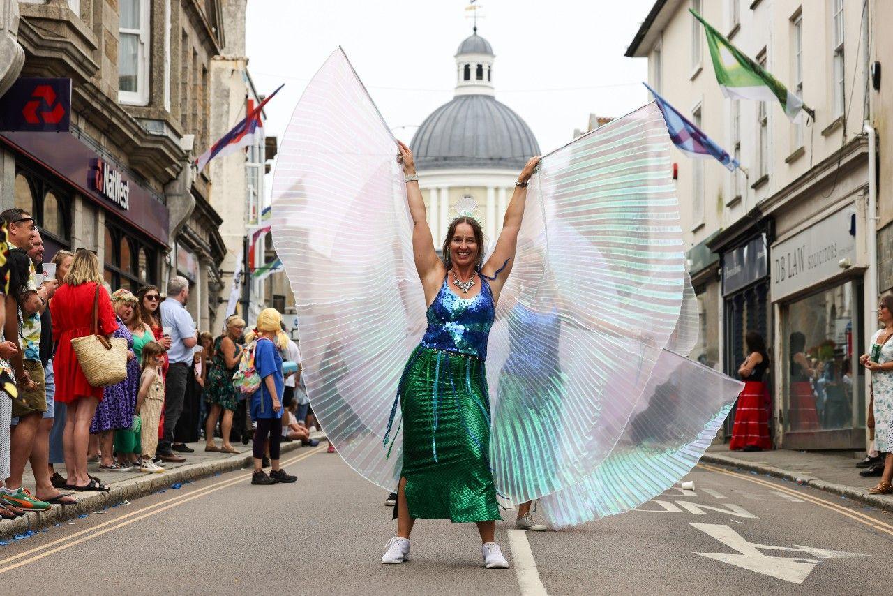 A woman in a blue and green sequined outfit and giant wings
