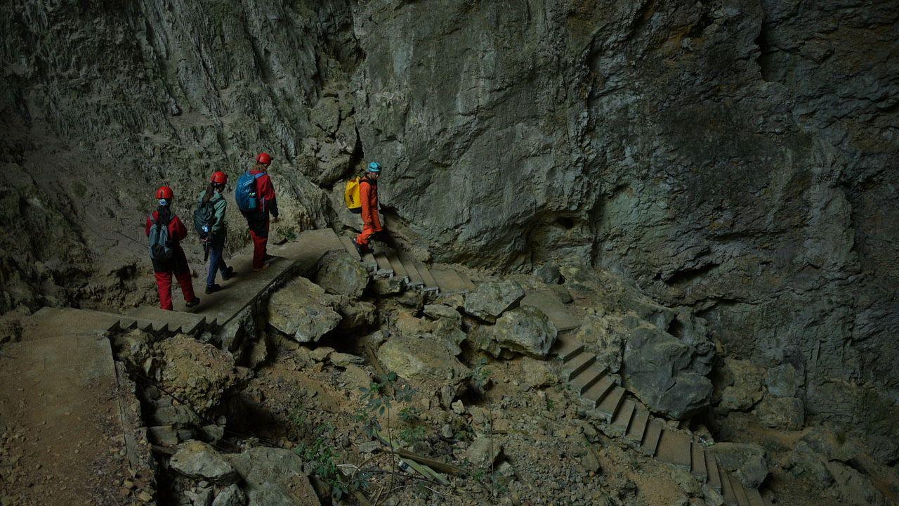 Four people climb down rock stairs into the hole