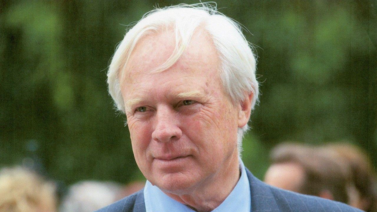 A close up shot of a blonde haired man in a blue pinstriped blazer and light blue shirt