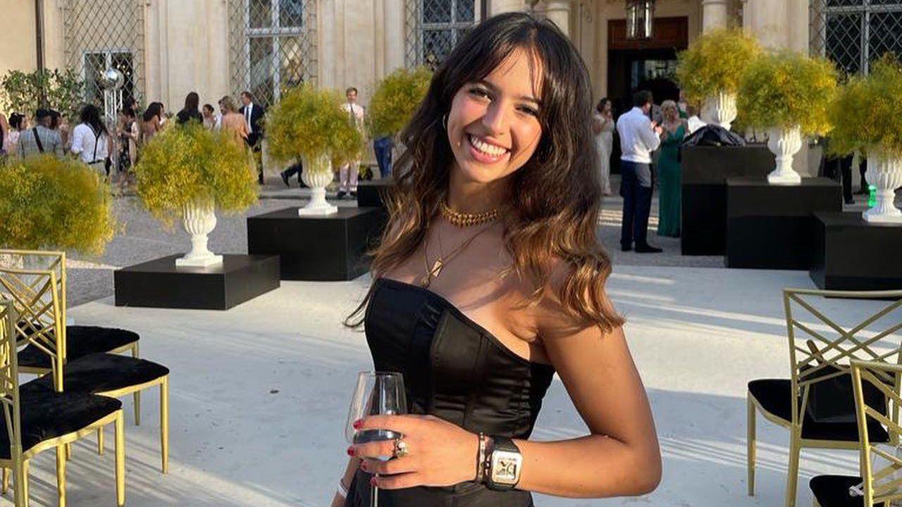 Grace O'Malley-Kumar smiling for the camera with long brown hair while holding a glass of wine at an outdoors event.