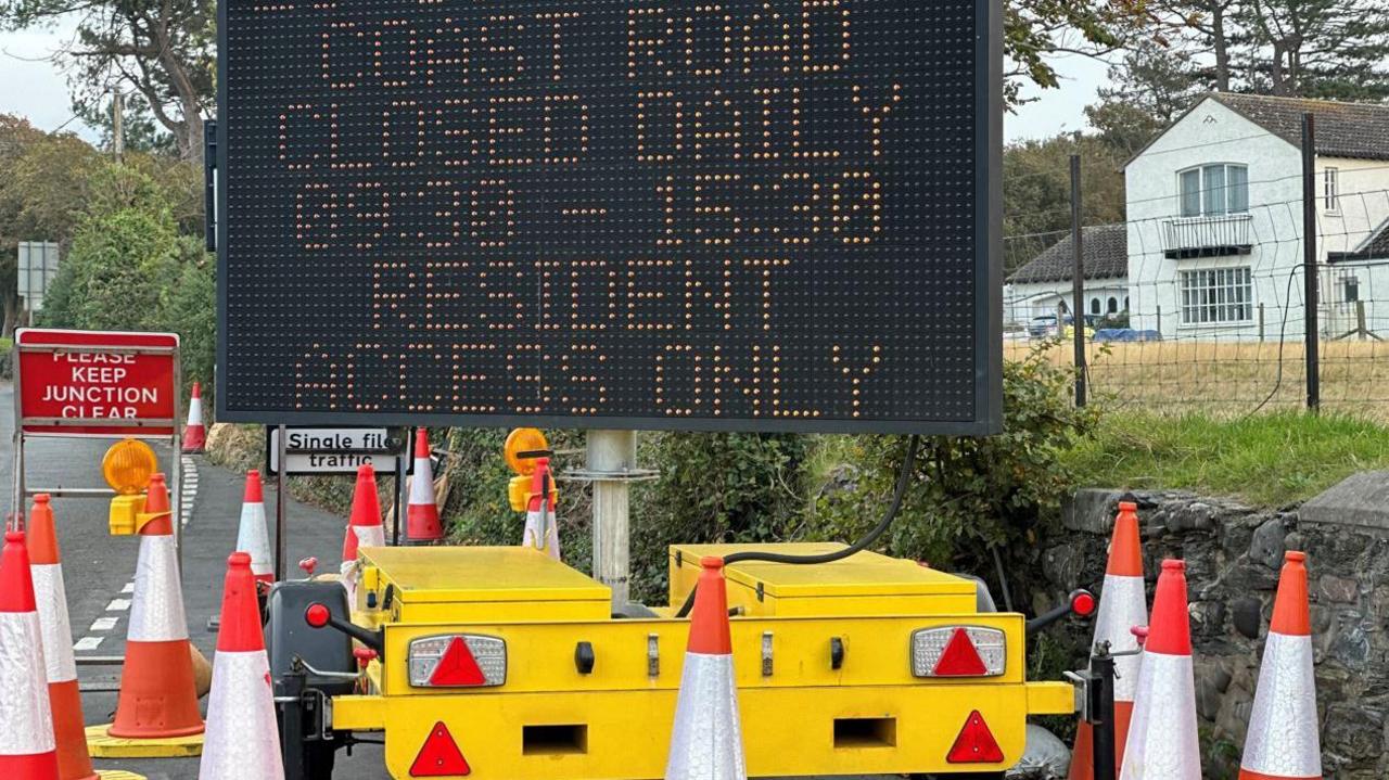 A large black matrix sign on a yellow trailer, which is surrounded by orange and white traffic cones, displaying details of the closure.