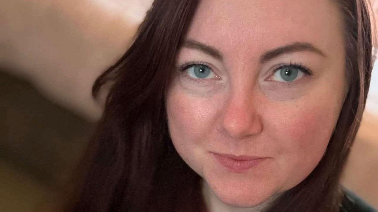 A close-up of a woman's face. She has grey eyes and long dark hair and a smile is playing on her lips.