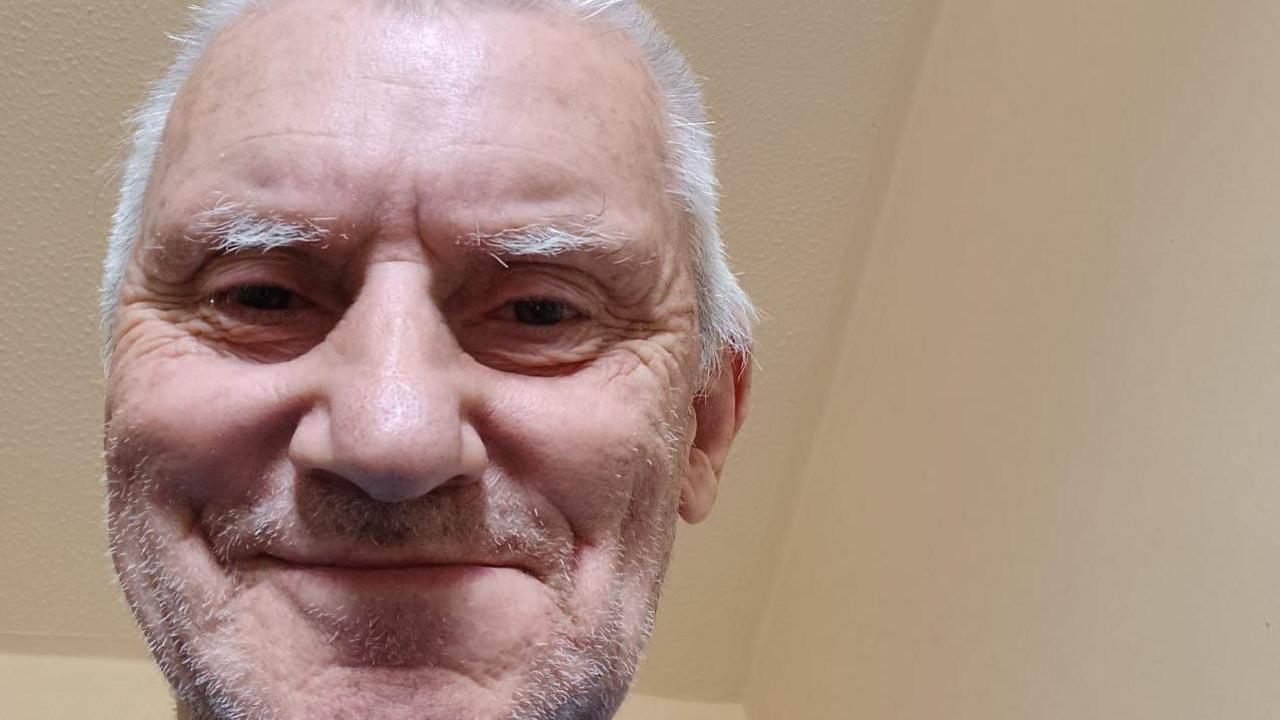 Bob smiles down at the camera in a selfie with a white ceiling in the background
