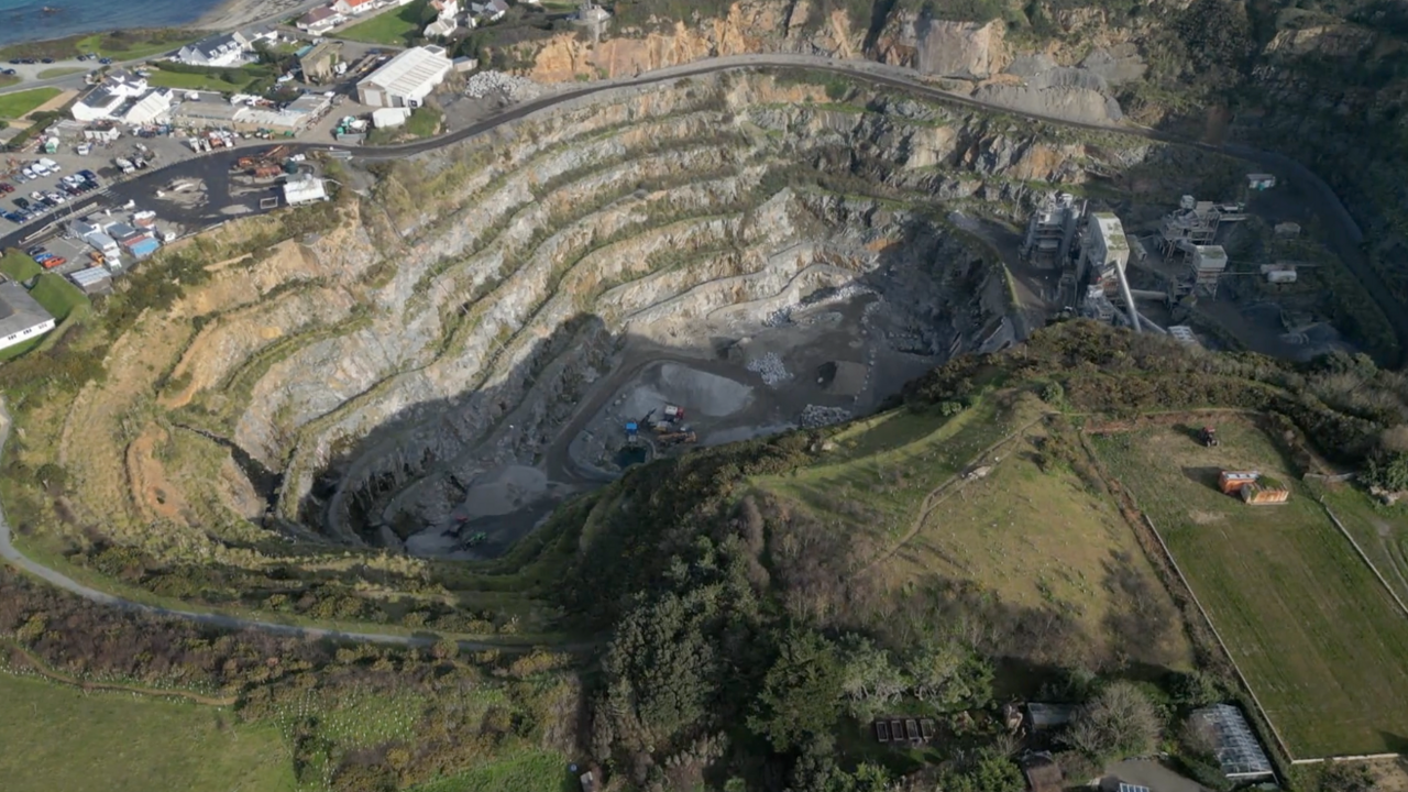 A birdseye view of Les Vardes Quarry. It is surrounded by green and there is also a car park. 