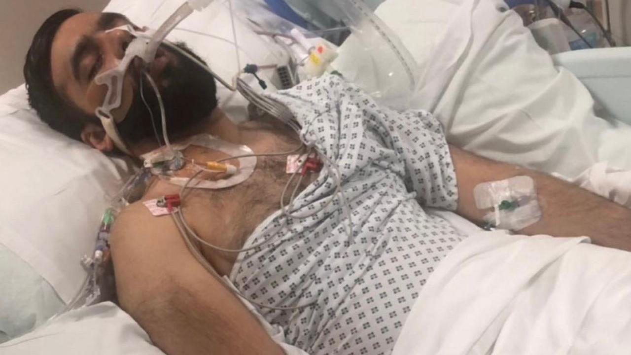 A man lies in a hospital bed hooked up to wires and drips.