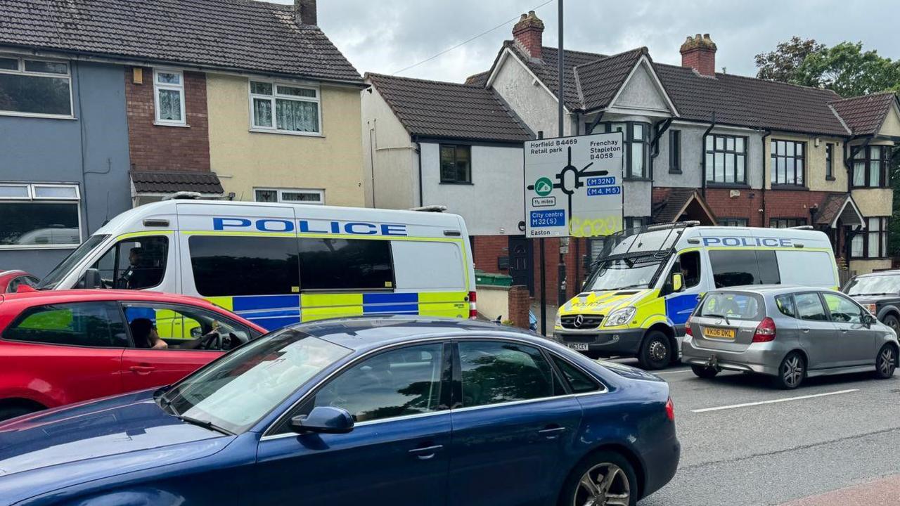 A picture of a busy road with two riot vans parked up 