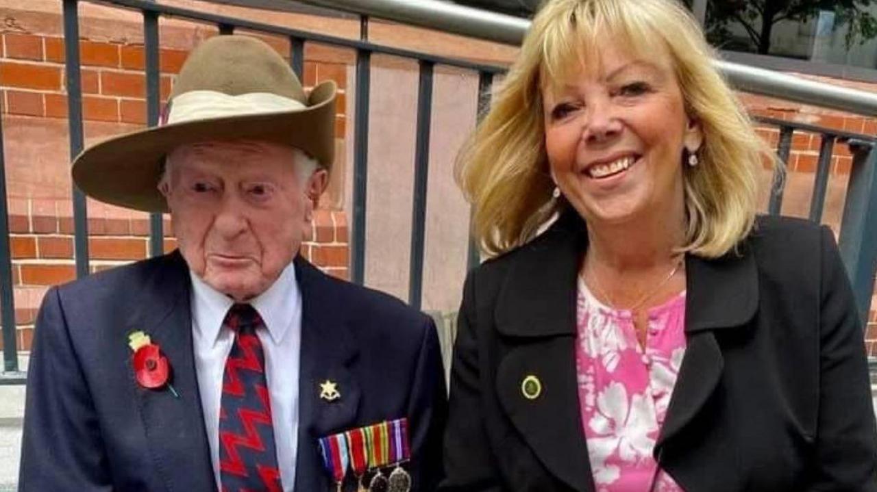 James Fenton, who is wearing a tan slouch hat with medals pinned to the pocket of a blue blazer, and a poppy pinned on the opposite side, alongside Sheila Healey, who is wearing a black jacket over a pink and white floral dress. 