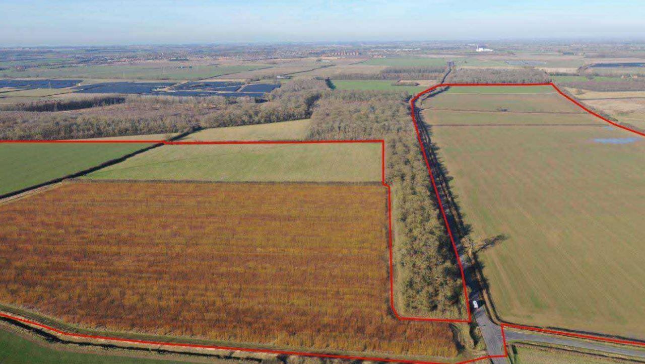 Aerial view of the proposed site. The outline is marked in red. There is a road running between the two marked areas and trees in the background.