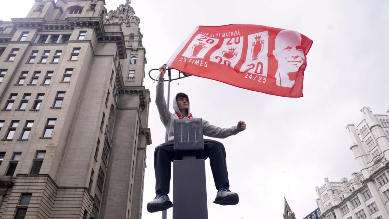 A Liverpool fan on top a piece of road furniture, waving a flag