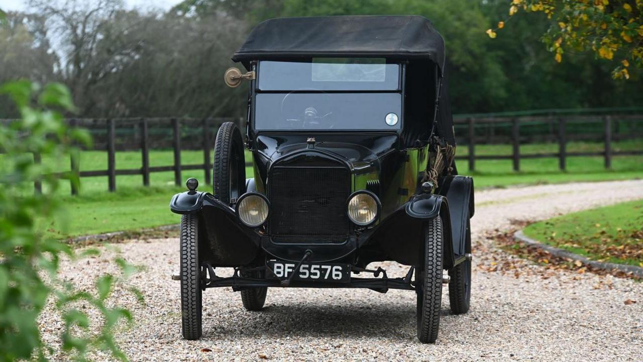 A black 1925 Ford Model T two-seat runabout being driven along a windy shingle driveway in the countryside 