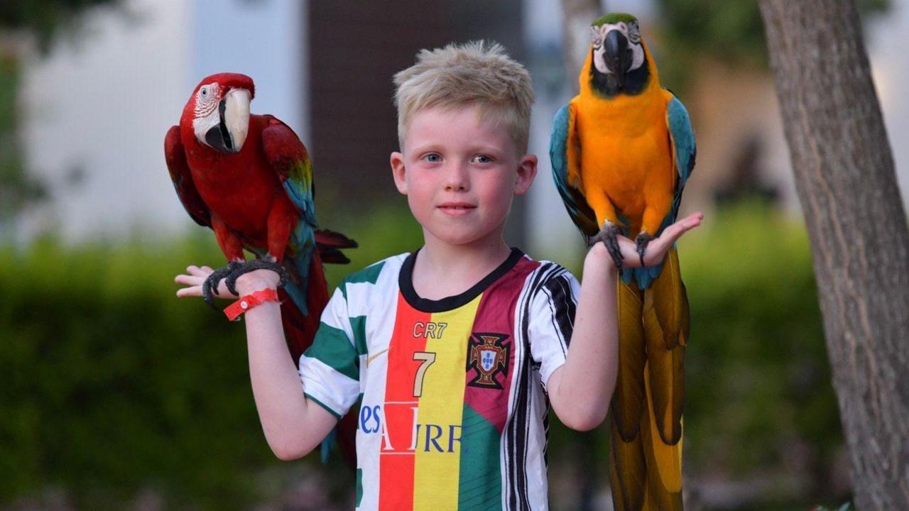 Louie on holiday. He is wearing a sports top and has a parrot perched on each hand.