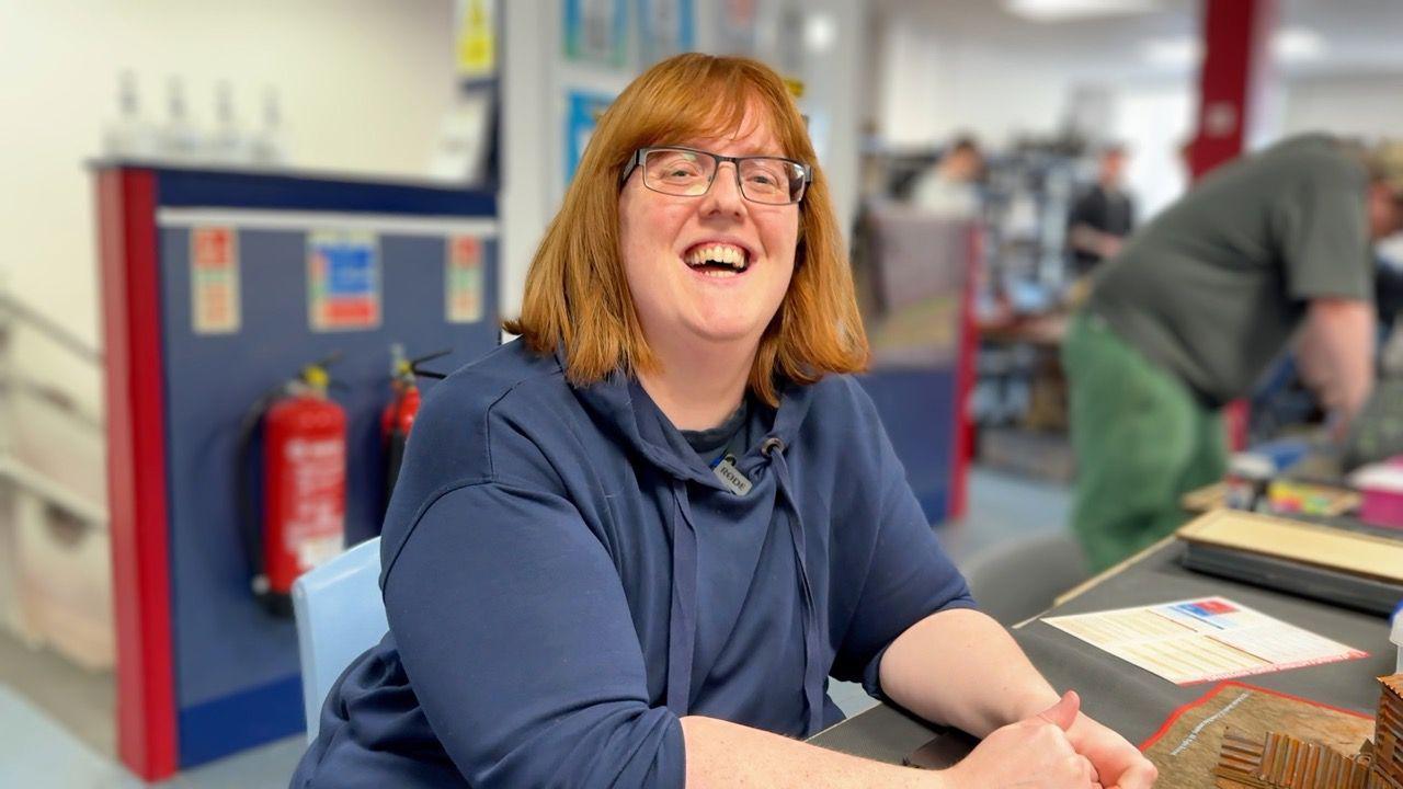 Amy Snuggs smiles and looks into the lens. She has ginger hair and wears a blue top and glasses.