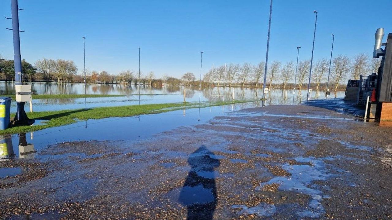 Wider shot of club pitches, with some hard surfaces flooded and much of a grass area flooded.