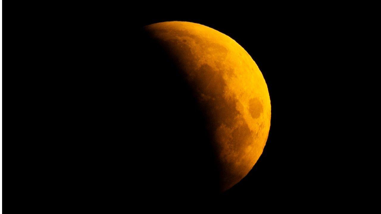 a yellowy-orange Moon almost completely obscured in darkness