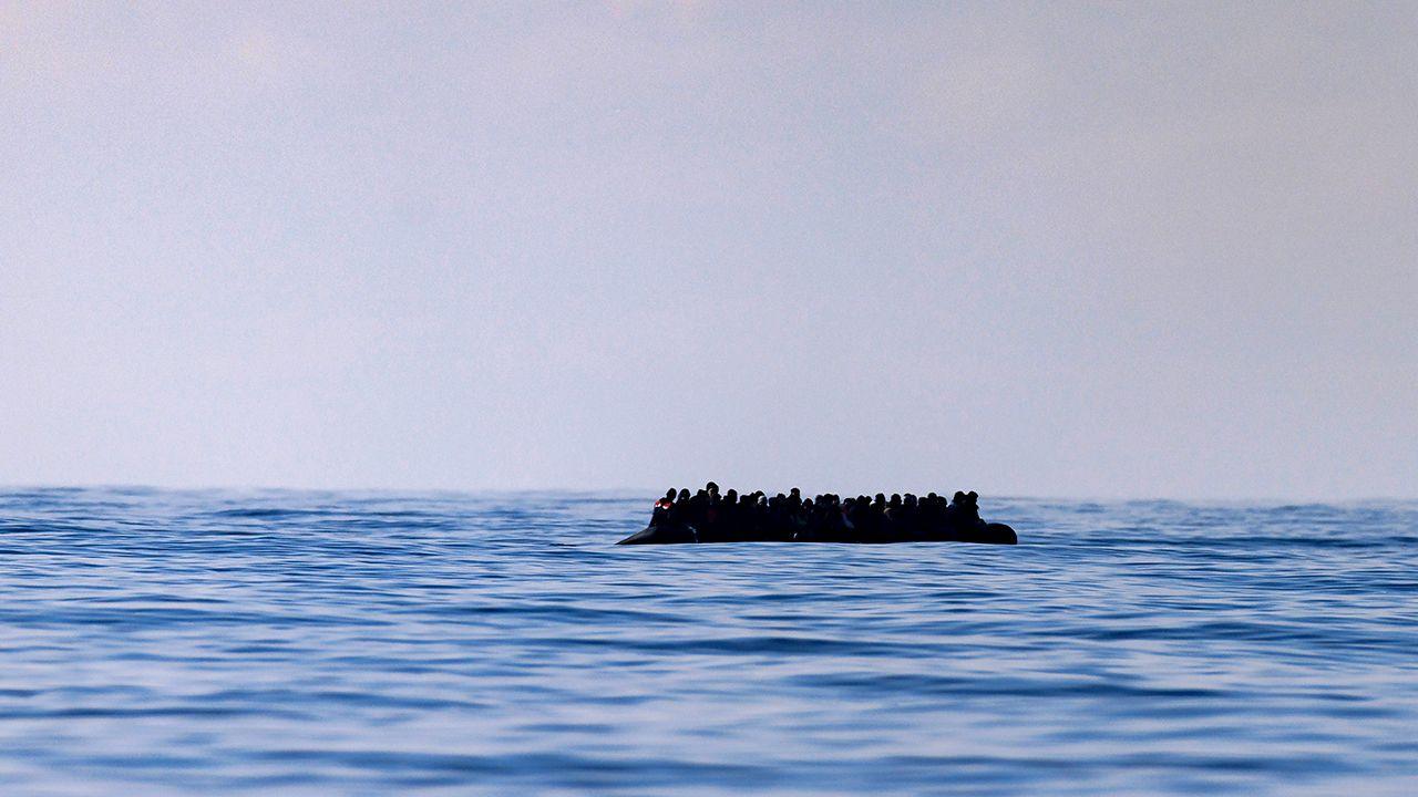 A inflatable dinghy carrying around 65 migrants can be seen silhouetted against a grey sky on a blue sea, as it crosses the English Channel in March