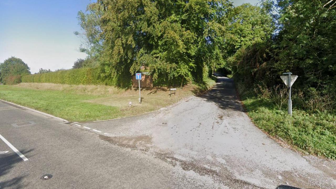 A Google screenshot of the Downs Lane junction opening up onto the A4. It is a long single carriageway rural road with thick trees lining either side. 