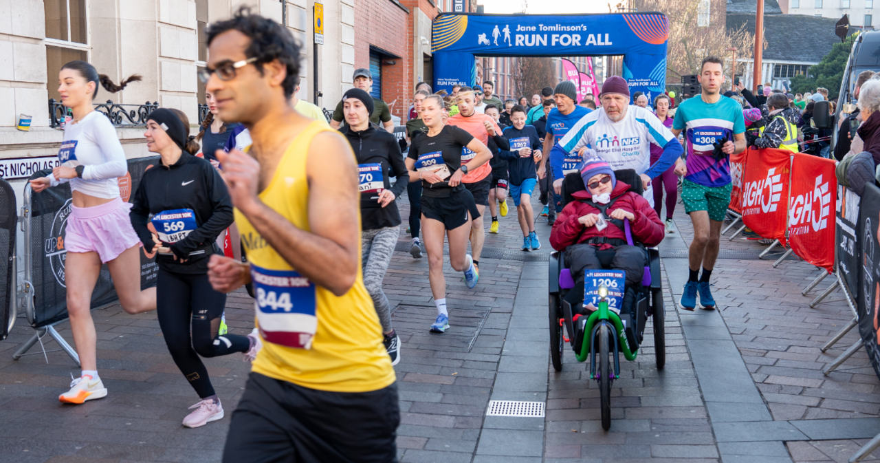 Runners one in yellow and man pushing a three-wheeled bicycle with Run for All banner in background