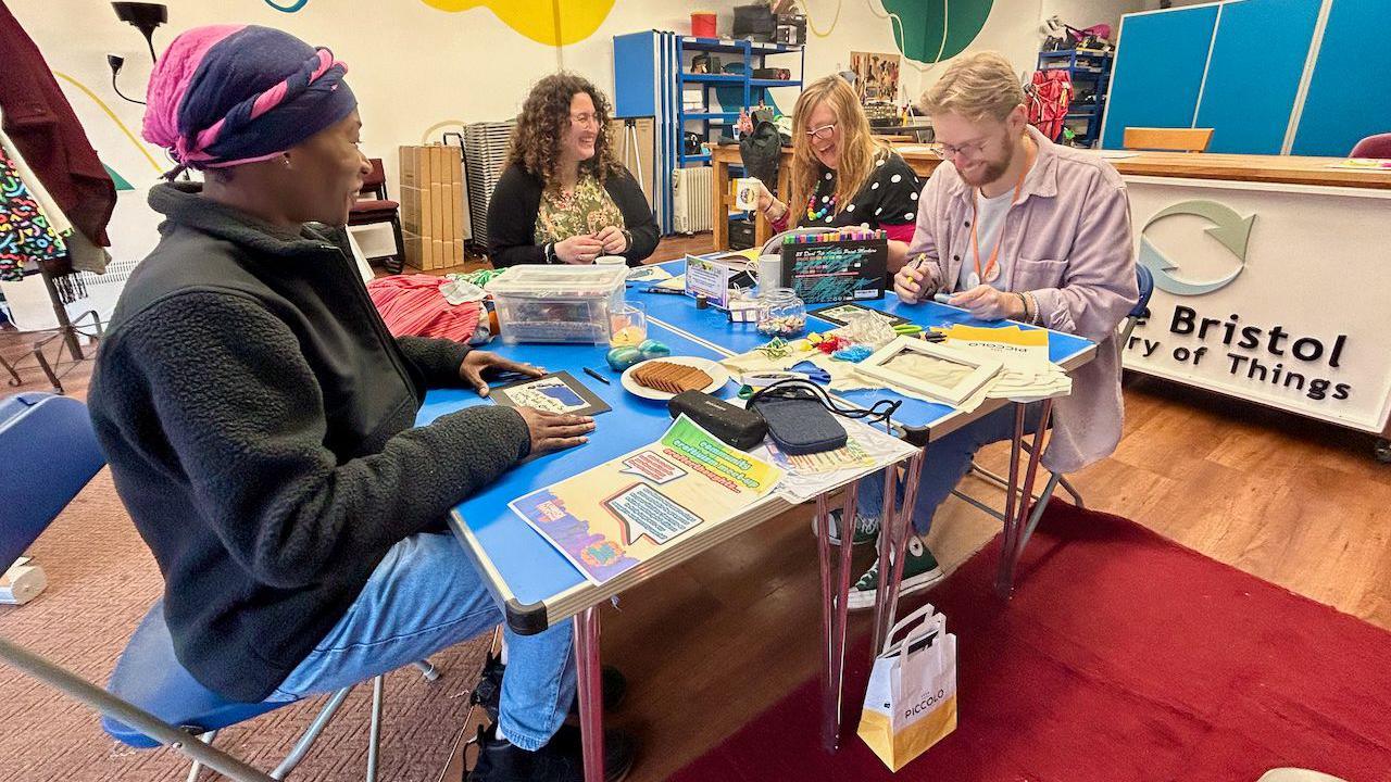 A group of four people sit around a table at a community centre in Bedminster in Bristol working with craft materials