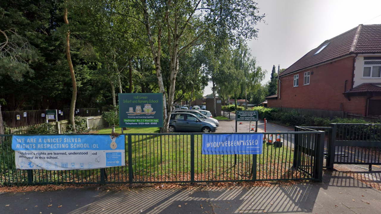 School gate, with a green school sign with owls on it, and a blue Unicef banner attached to the fence