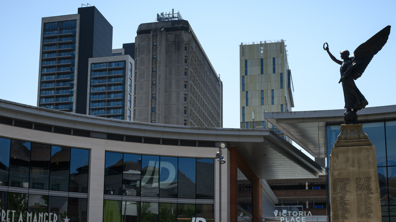 Victoria Place in Woking, with a statue and tower blocks outlined against a bright blue sky.