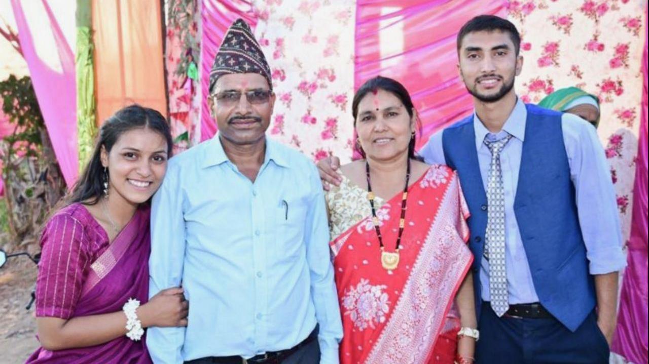 The Joshi family stands in a row smiling at the camera, with several coloured sheets as a backdrop