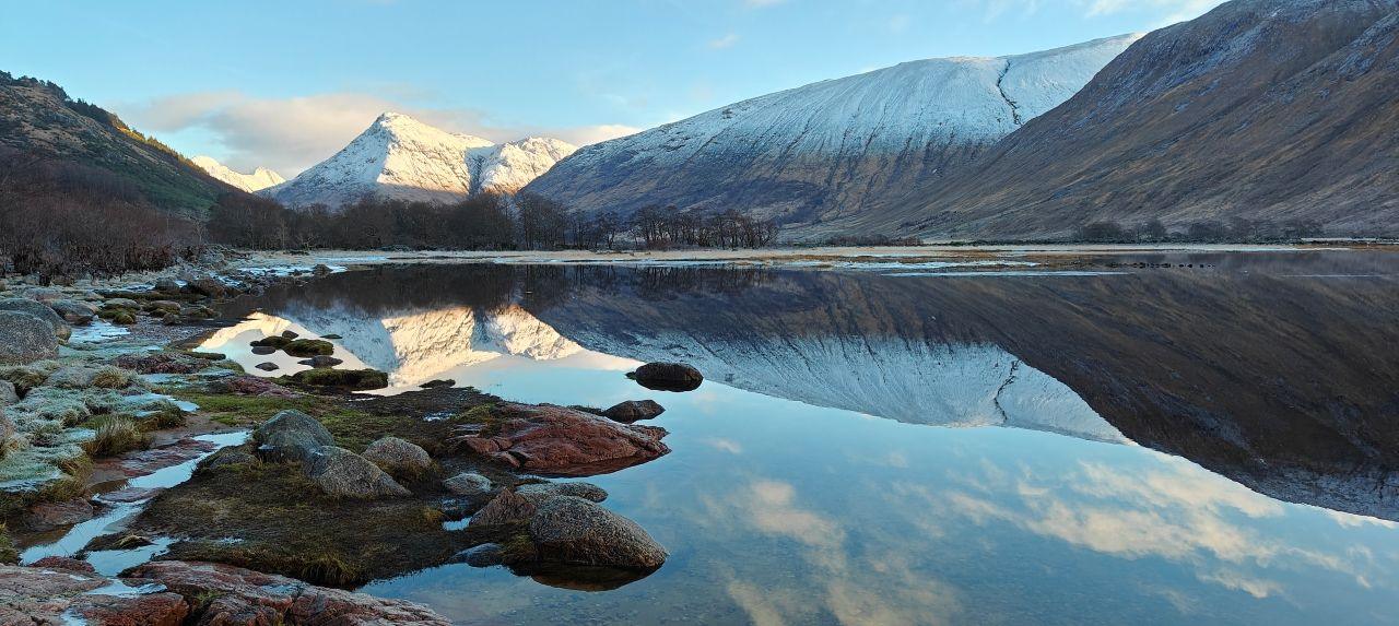 A body of clear water, with hills in the background reflected in the water