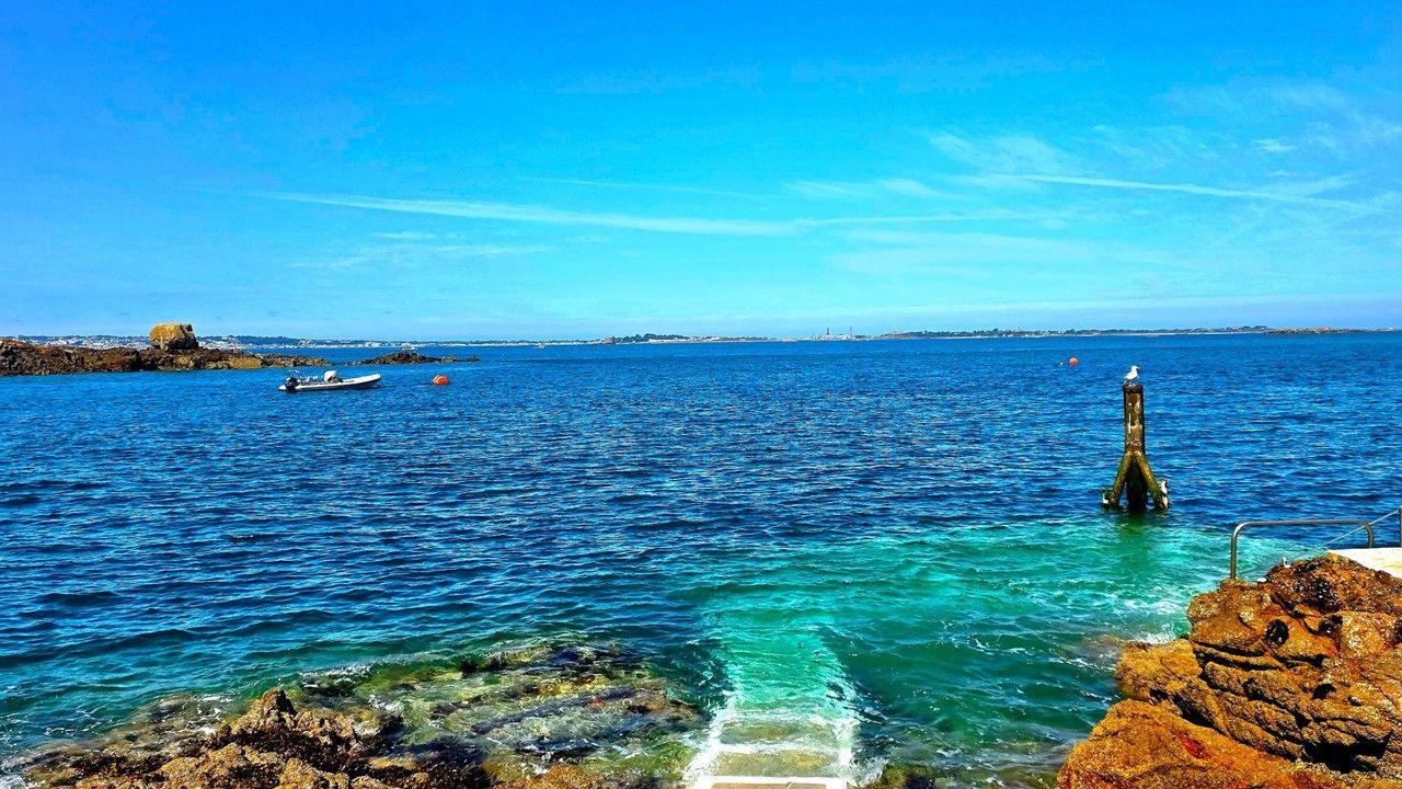 Aquamarine sky over blue sea, which turns green by the rocks in the foreground