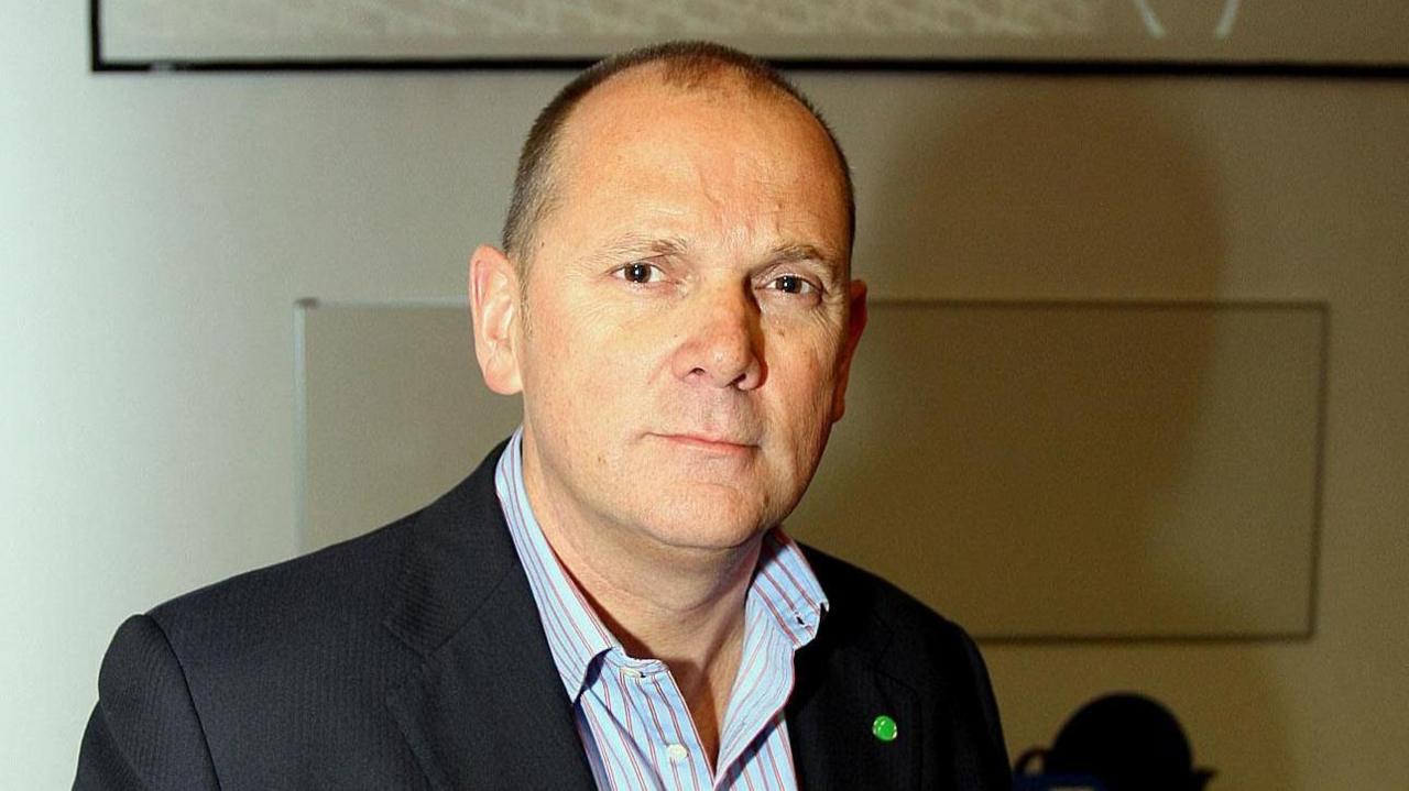 Jim Gamble, wearing a black blazer and a striped shirt