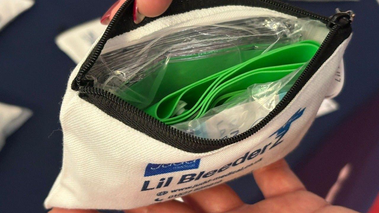 A white bag has its zip open and items are inside.