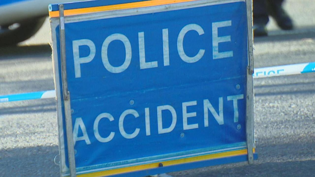 Police accident sign with white block capitals on blue sign, with road behind.