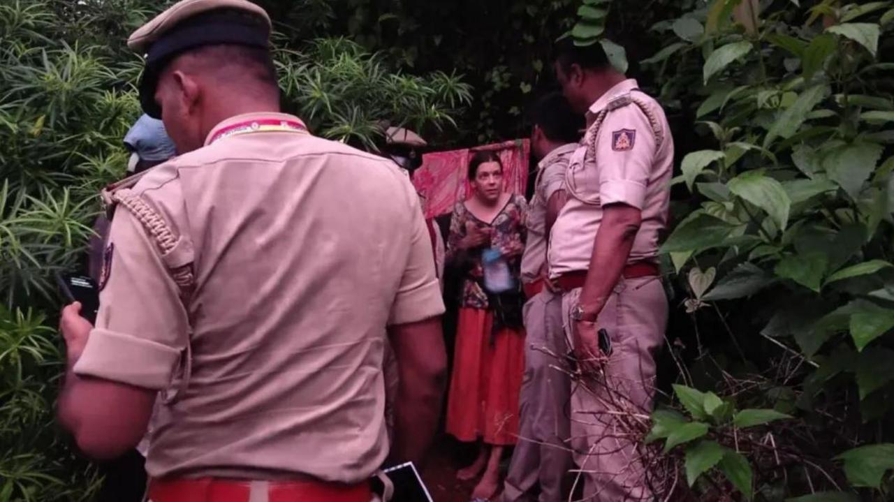 Nina Kutina comes out of the cave, wearing a floral print top and a red skirt, in a forest in Karnataka's Gokarna, as a team of policemen un uniform surround her