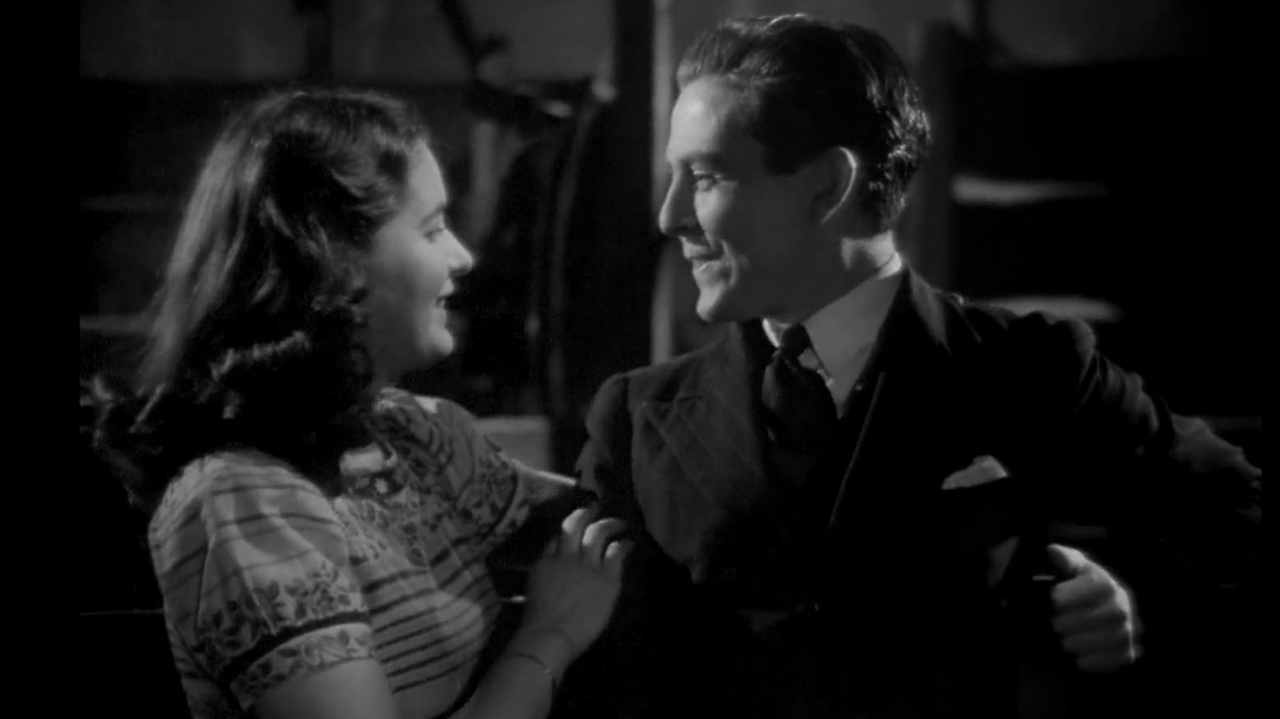 A black and white still from I Know Where I'm Going of actors Margot Fitzsimons and Murdo Morrison standing close to each and looking into each other's eyes.