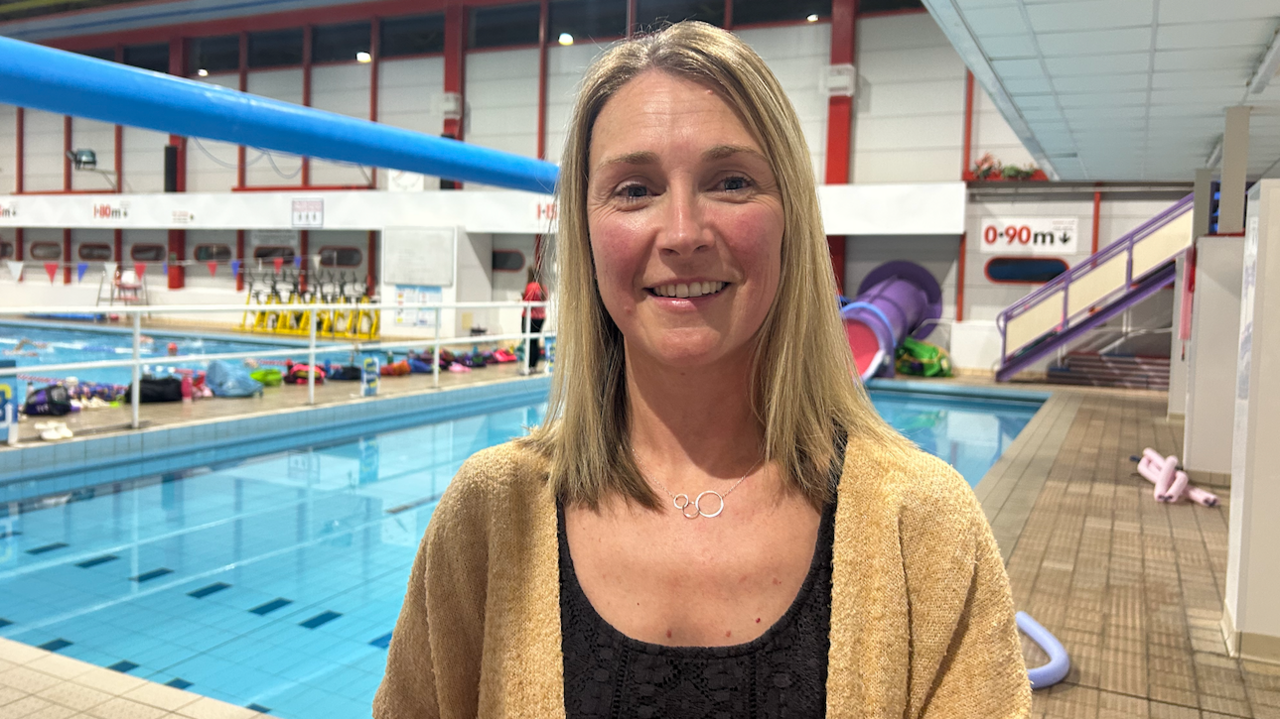 Nicola Morris in a black top and beige cardigan, smiling, pictured in front of a swimming pool.