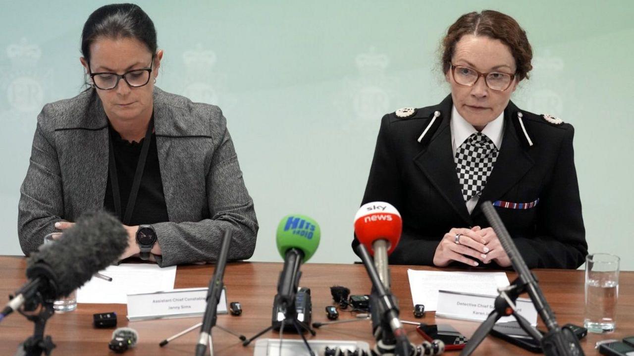 Detective Chief Superintendent Karen Jaundrill and Assistant Chief Constable Jenny Sims from Merseyside Police are sitting at a desk while speaking during a press conference at police headquarters. There are a number of microphones from media outlets positioned on the desk in front of them.