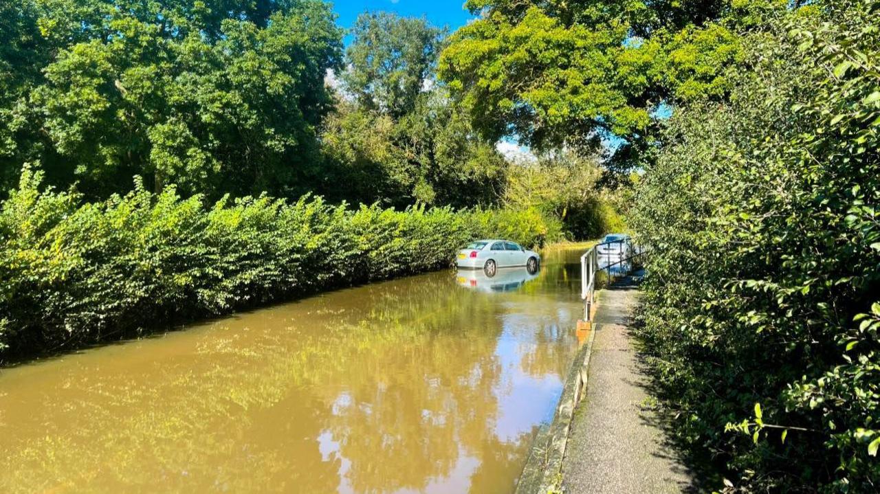 A stretch of flooded road with cars stopped in it