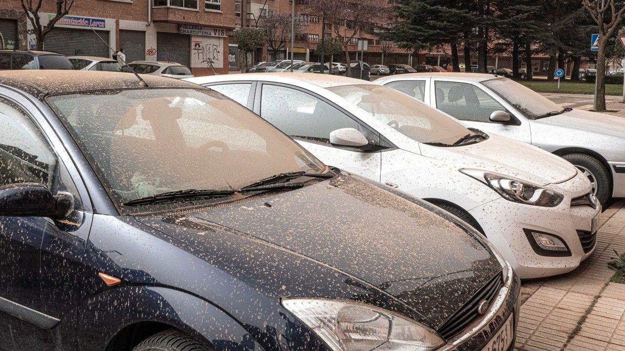 Row of three cars covered with reddish dust, known as 'blood rain'