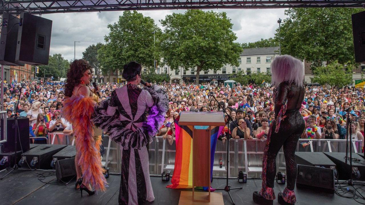 Performers wearing colourful clothes on stage in Sneinton. A large crowd is in attendance.