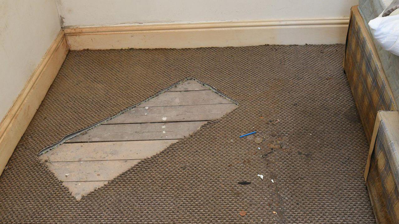 Rectangular piece of carpet beige carpet cut out of the floor in a room at a house.