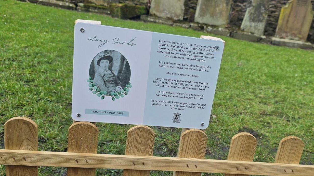 The small memorial plaque with a black and white picture of Lucy Sands on the left and some words to describe who she was on the right.