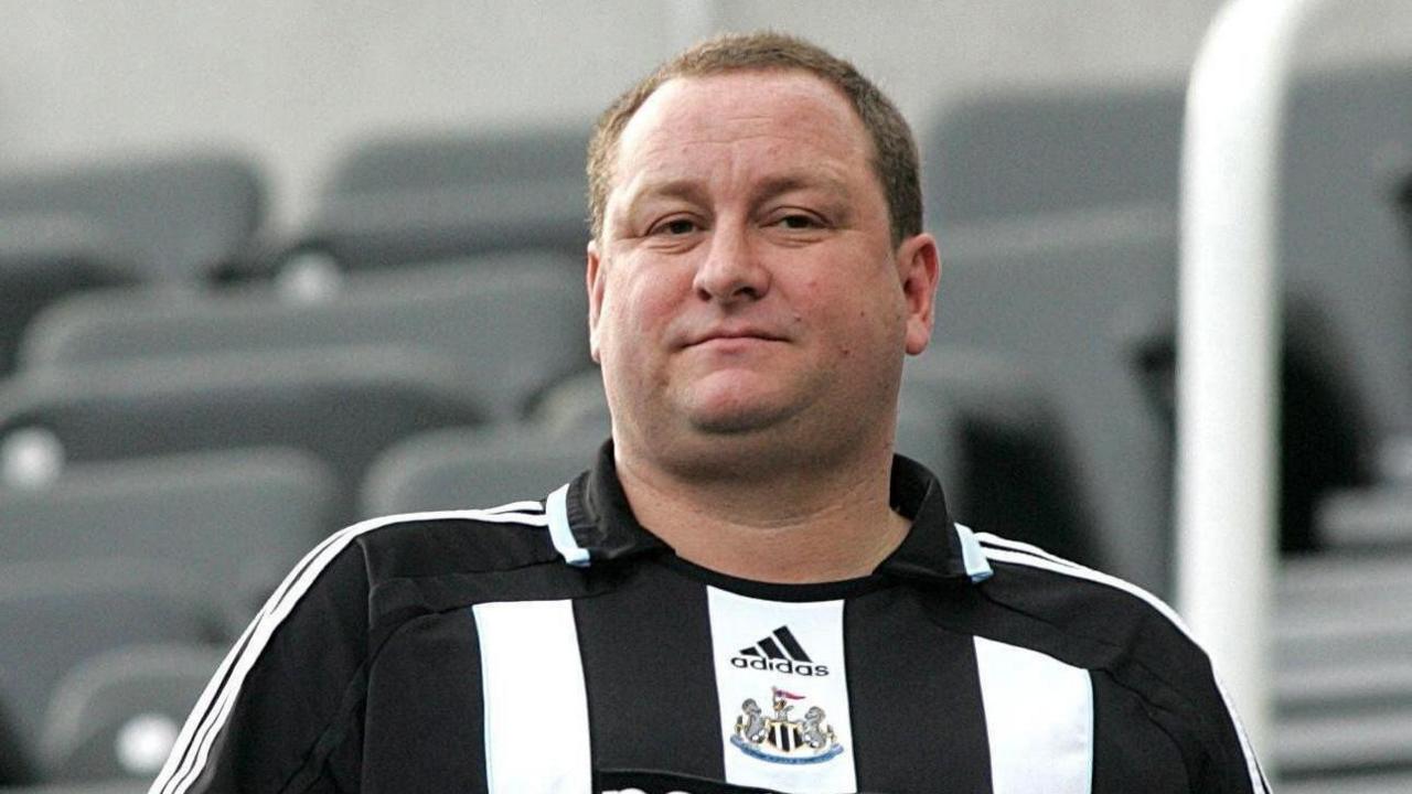 Mike Ashley wears a Newcastle United shirt. He has short-cut brown hair and is clean shaven.