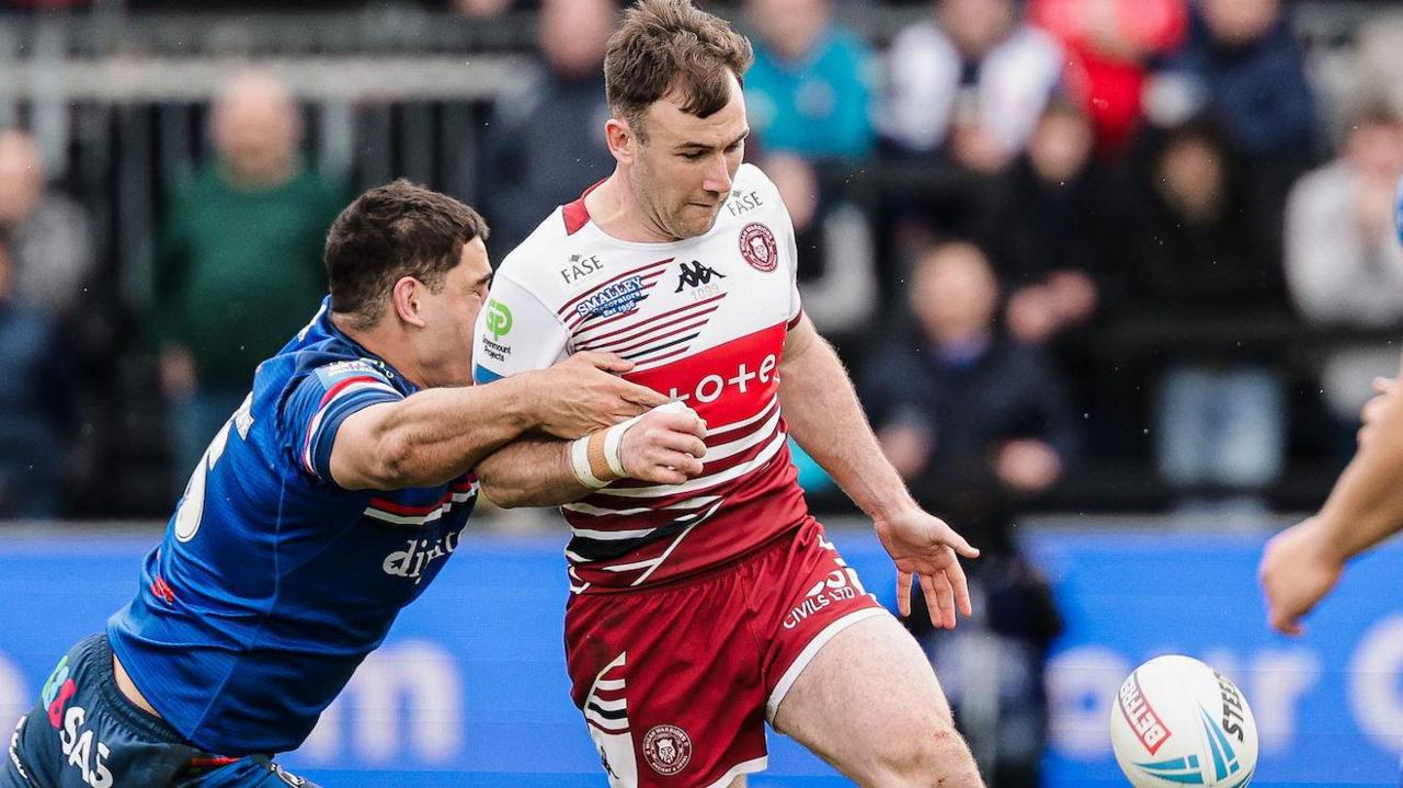 Wigan Warriors' Harry Smith (centre) kicks the ball during their Challenge Cup game at Wakefield as an opposing player tries to make a tackle