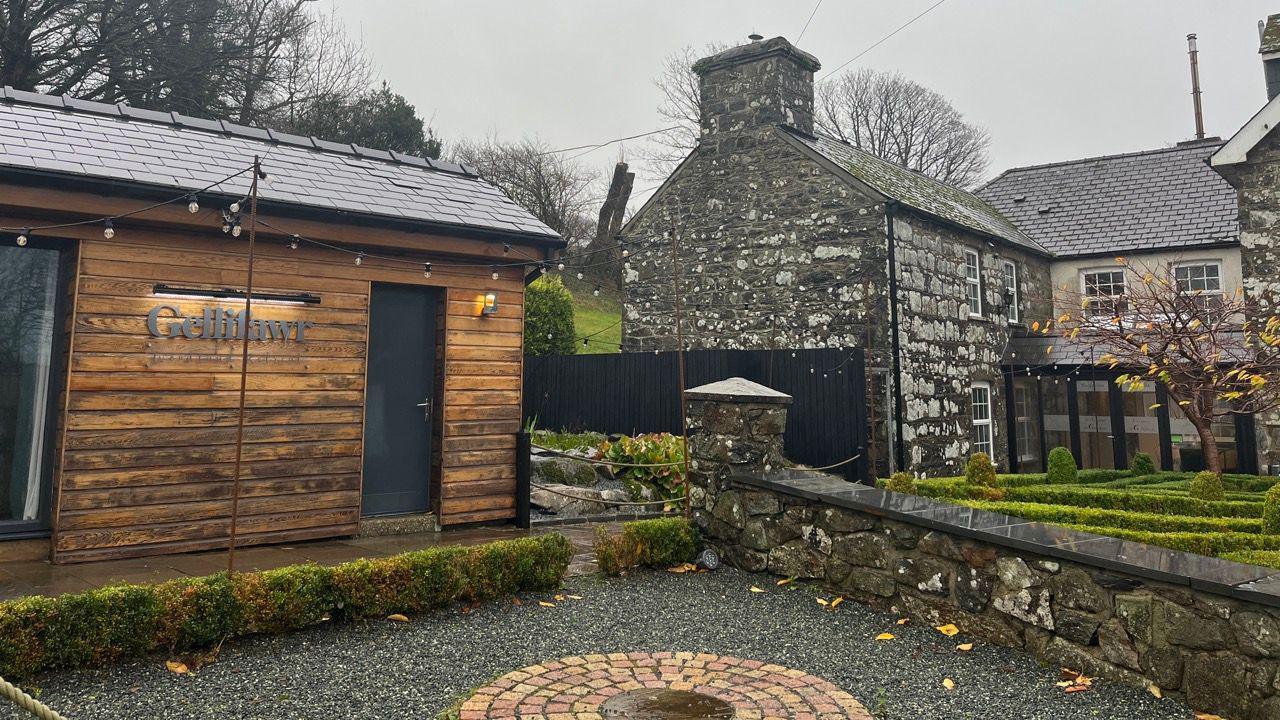 Llun o westy Gellifawr. Ar y dde mae yna adeilad sydd wedi'i adeiladu gyda cherrig. O flaen yr adeilad mae yna ardd fach gydag un goeden ynddi sydd wedi colli rhan fwyaf o'i dail. I'r chwith mae yna adeilad pren sydd gyda'r enw Gellifawr arno.