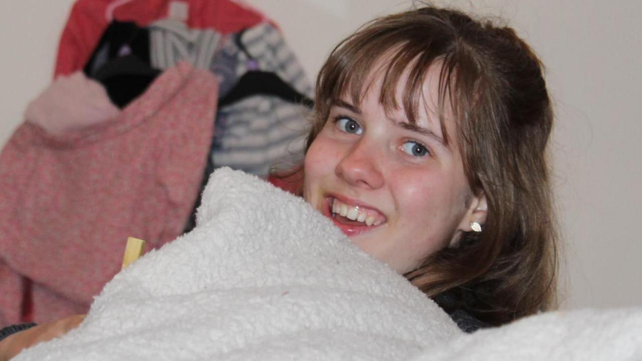 A photograph of Alex smiling from behind a grey blanket.