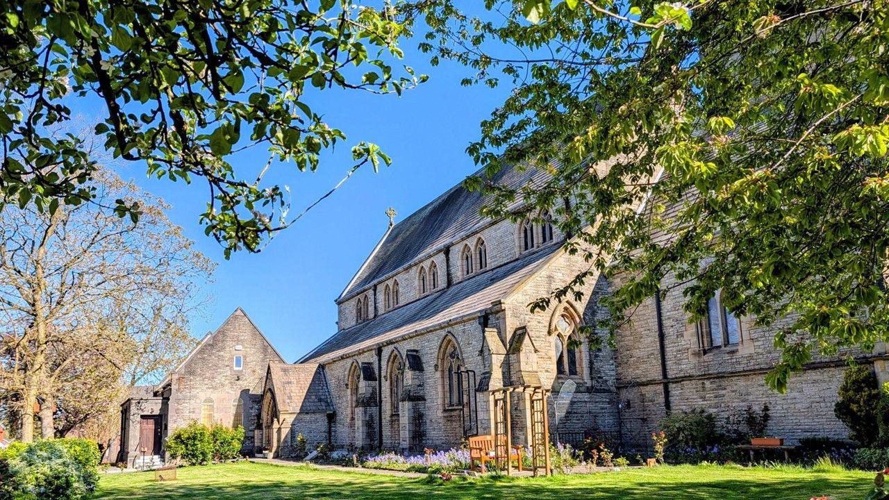Old church bathed in sunlight with tree branches and clear blue sky.