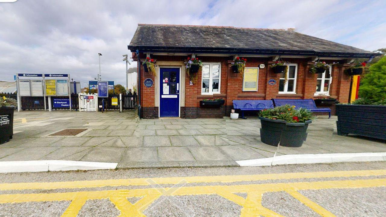 The entrance to St Annes Railway Station showing flower pots outside the ticket office building with signs with timetables to the right of the turnstile to the platform.