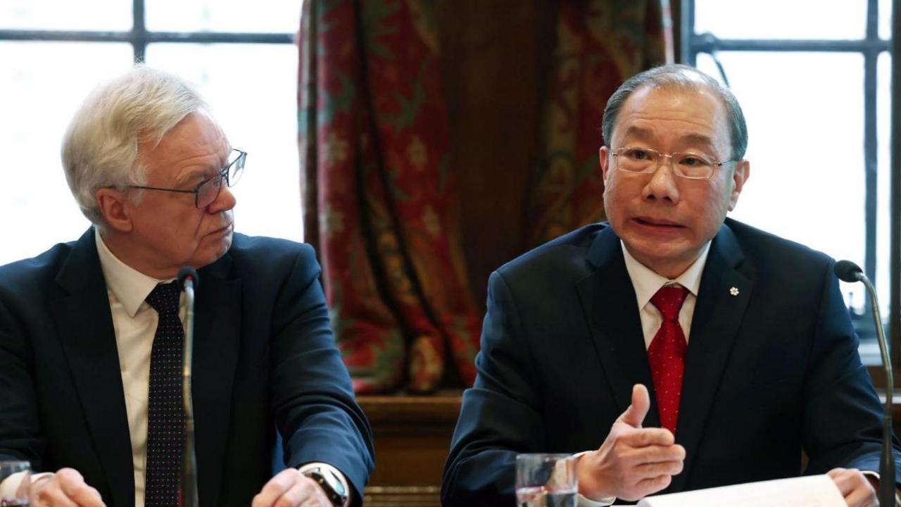 Conservative MP David Davis and Professor Dr Shoo Lee sit side-by-side at a press conference to unveil new evidence on the Lucy Letby case. They are both older men, wearing dark suits. The MP is wearing a dark tie, Dr Lee is wearing a red tie and has papers and a glass of water in front of him.