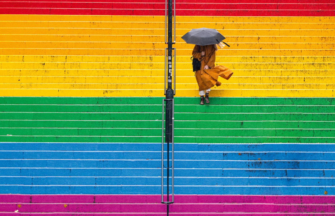 Colourful steps in a rainbow effect with a lady with an umbrella walking down